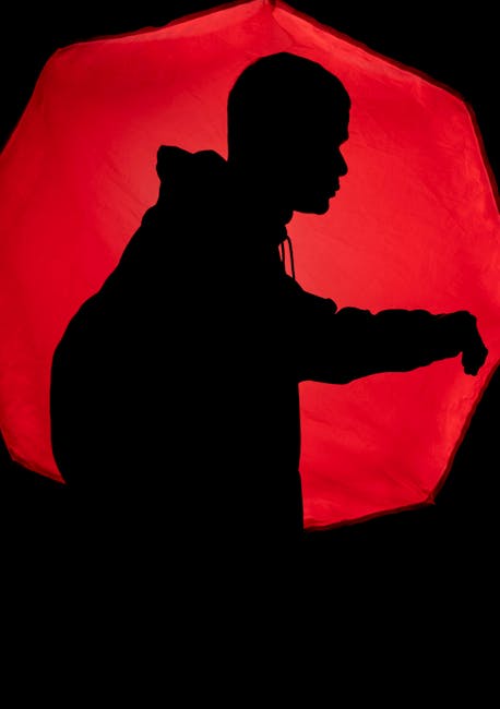 Silhouette of person meditating in lotus pose against vibrant sunrise backdrop.