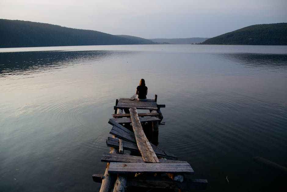 Woman practicing yoga on a wooden pier with calm lake view at sunset.